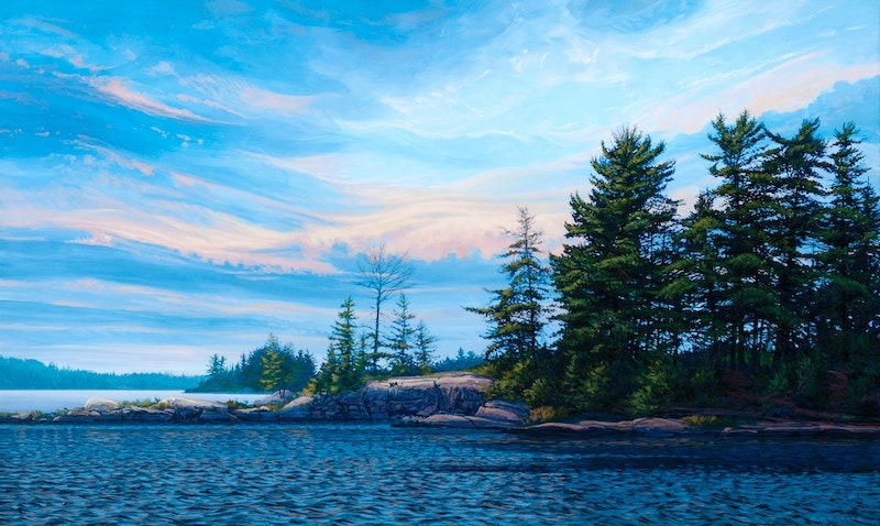 Image of the archival pigment print of Upper Corkscrew Channel (2022) by Randolph Parker. The image shows a serene landscape, approaching twilight. Shades of vibrant blues and light pink wave through the sky, which takes up 3/4 of the painting. Dark  green trees stand tall to the right of the painting, over a rocky shore. The lake below it is calm, but dark, suggesting a sunset occurring behind the viewer. 